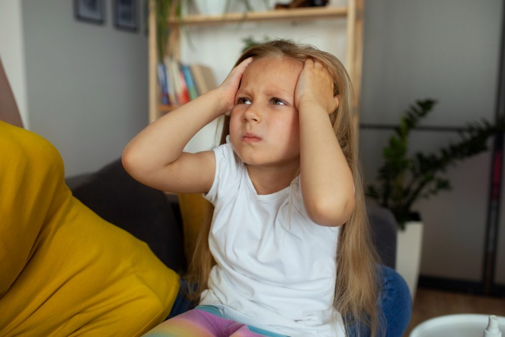Frustrated young girl holding her head, showing signs of ADHD and anger in kids.