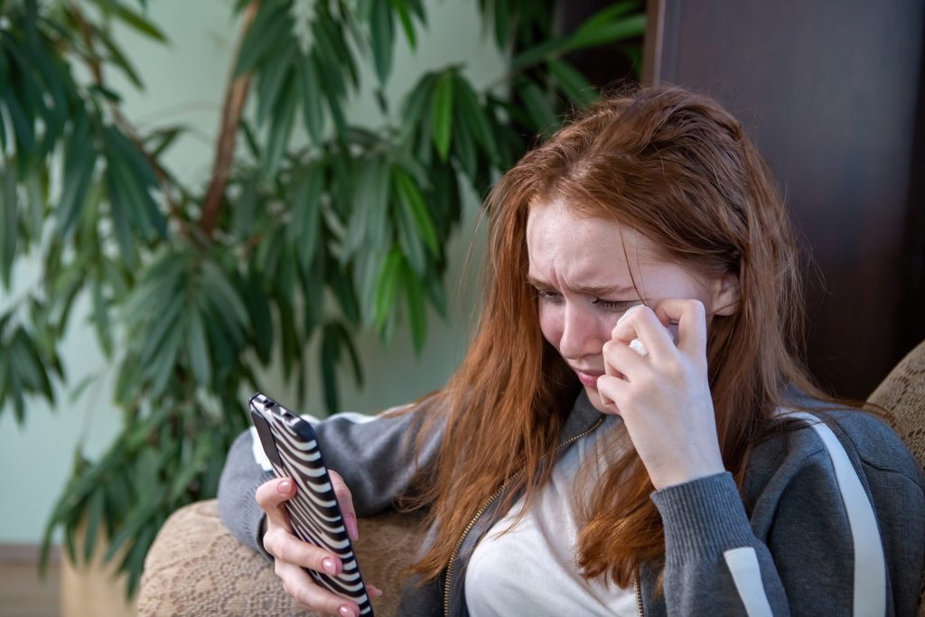 Effects of technology on mental health shown as young woman upset while using phone