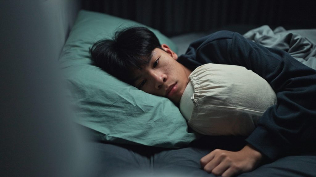 Young man lying awake in bed struggling with insomnia, illustrating the need for cognitive behavioral therapy for insomnia